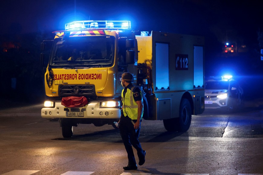 A police officer walks next to an emergency service truck during a wildfire in Tres Cantos, near Madrid, Spain, August 11, 2025. REUTERS/Juan Medina