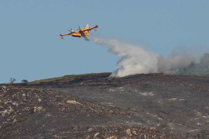 An aircraft makes a water drop over an area burned by a wildfire in the Atlanterra area in Tarifa, Spain, August 12, 2025. REUTERS/Marcelo Del Pozo