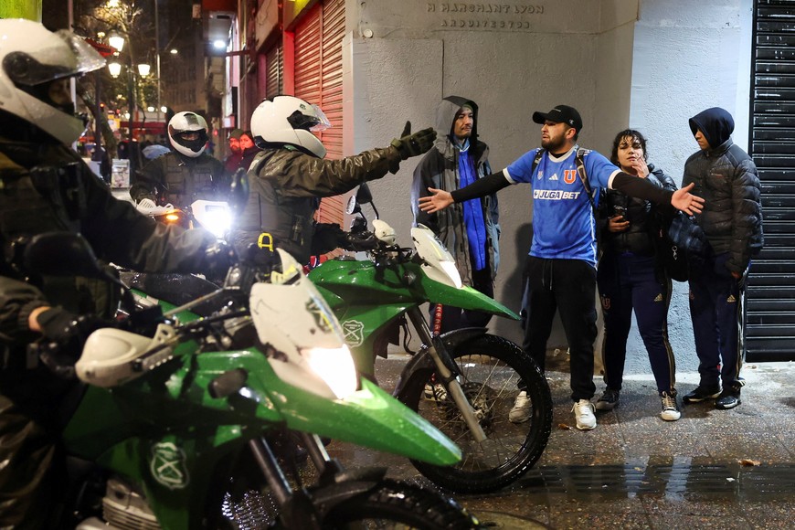 Police officers ask Universidad de Chile fans to leave as they gather near the Argentina's embassy after fellow fans were detained in Argentina following clashes with Independiente supporters, during the second leg of the Copa Sudamericana Round of 16 match, which was suspended due to violence in the stands, in Santiago, Chile August 21, 2025. REUTERS/Pablo Sanhueza