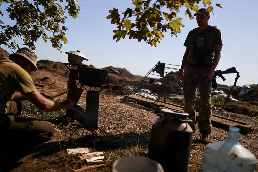 An Ukranian serviceman cooks as his mate looks him near the firing point, as Russia's invasion of Ukraine continues, in Kharkiv, Ukraine August 7, 2022. REUTERS/Nacho Doce
