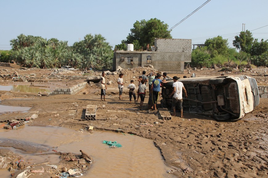 People stand by a van that was overturned by floods in Al-Haswa suburb of Aden, Yemen August 24, 2025. REUTERS/Fawaz Salman