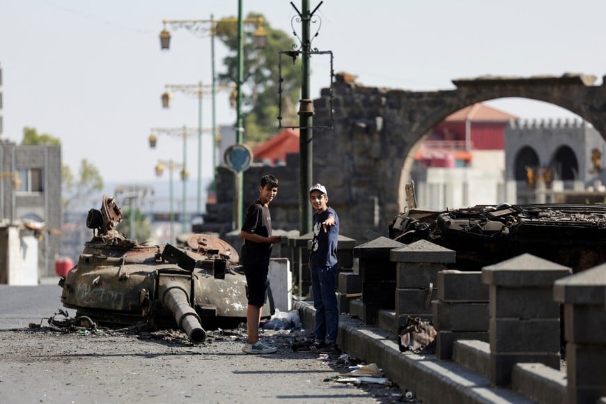 People stand next to a destroyed tank, following deadly clashes between Druze fighters, Sunni Bedouin tribes and government forces, in Syria's predominantly Druze city of Sweida, Syria July 25, 2025. REUTERS/Khalil Ashawi