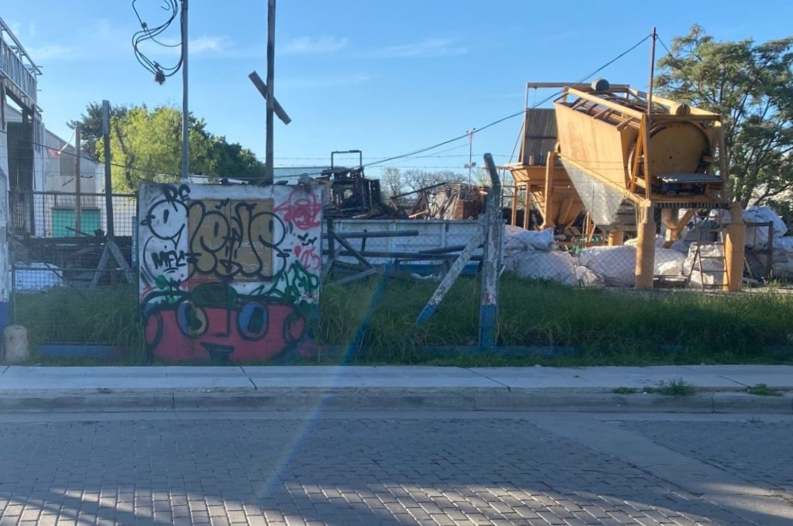 Bloque grafiteado y máquinas detrás: postal cruda del borde industrial. 