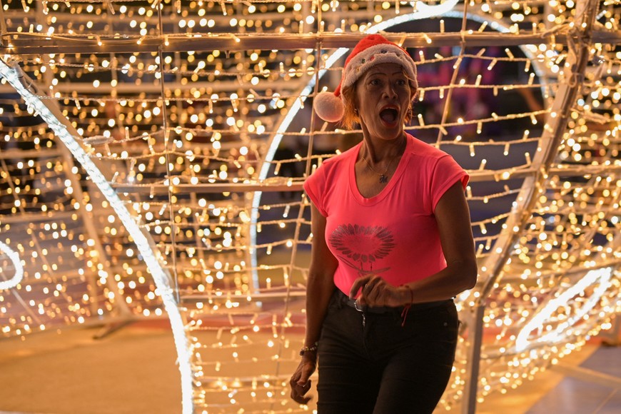 A woman reacts as she poses with Christmas decorations in a public square as the holiday season officially begins since Venezuela's President Nicolas Maduro announced that Christmas celebrations would start in October, two months ahead of the traditional season, in Caracas, Venezuela October 1, 2025. REUTERS/Gaby Oraa