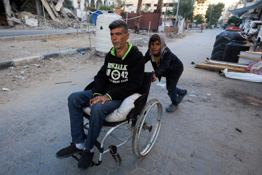 A Palestinian boy pushes a man on a wheelchair on a street next to damaged buildings, amid a ceasefire between Israel and Hamas, in Gaza City, October 14, 2025. REUTERS/Dawoud Abu Alkas TPX IMAGES OF THE DAY
