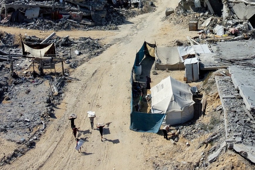 Palestinians walk past a tent amid the rubble in a destroyed area, amid a ceasefire between Israel and Hamas in Gaza, in Gaza City, October 19, 2025. REUTERS/Dawoud Abu Alkas     TPX IMAGES OF THE DAY