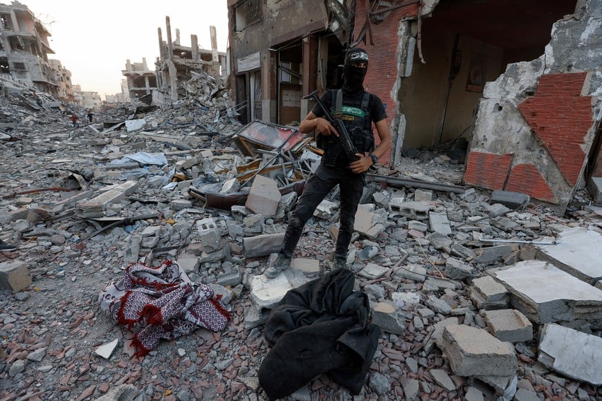 A Palestinian Hamas militant stands next to covered human remains amid rubble, after Hamas said that it found the body of an Israeli hostage soldier on Tuesday and prepares to return it to Israel through the Red Cross, in Gaza City, November 4, 2025. REUTERS/Dawoud Abu Alkas