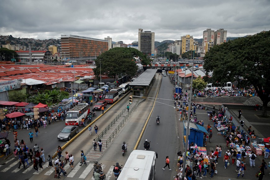 People walk across a street as others shop at a market, after U.S. President Donald Trump said on Saturday that the airspace above and around Venezuela would be closed entirely, amid rising tensions between the Trump administration and the government of Venezuelan President Nicolas Maduro, in Caracas, Venezuela, November 29, 2025. REUTERS/Leonardo Fernandez Viloria