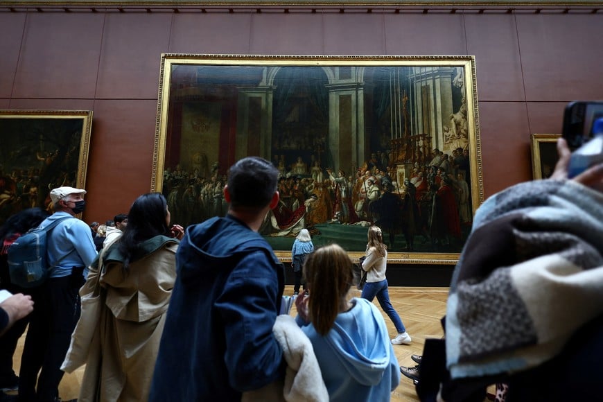 Visitors look at the painting "Le Sacre de Napoleon" (Le Couronnement de l'empereur Napoleon Ier et de l'imperatrice Josephine dans la cathedrale Notre-Dame de Paris, le 2 decembre 1804) by French artist Jacques-Louis David in the salle Mollien of Denon wing at the Louvre Museum on the day it reopened to the public for the first time since last Sunday's heist, while the Galerie d'Apollon where eight pieces of Napoleon and the Empress's jewelry collection displayed in the gallery were stolen by thieves, remains closed, in Paris, France, October 22, 2025. REUTERS/Gonzalo Fuentes