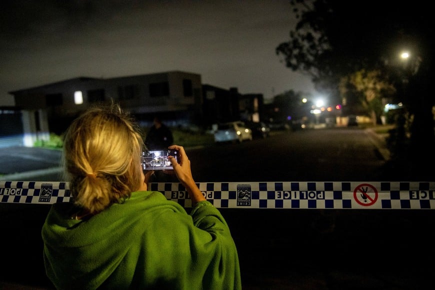 A woman records on her mobile phone as a police crime scene is established at the home of a suspect in Bonnyrigg, following a deadly shooting at Bondi Beach, in Sydney, Australia, December 14, 2025. AAP/Jeremy Piper/via REUTERS    ATTENTION EDITORS - THIS IMAGE WAS PROVIDED BY A THIRD PARTY. NO RESALES. NO ARCHIVE. AUSTRALIA OUT. NEW ZEALAND OUT. NO COMMERCIAL OR EDITORIAL SALES IN NEW ZEALAND. NO COMMERCIAL OR EDITORIAL SALES IN AUSTRALIA.