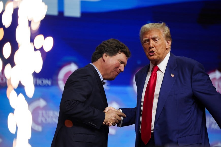 Republican presidential nominee and former U.S. President Donald Trump shakes hands with Tucker Carlson at a campaign event sponsored by conservative group Turning Point USA, in Duluth, Georgia, U.S., October 23, 2024. REUTERS/Carlos Barria