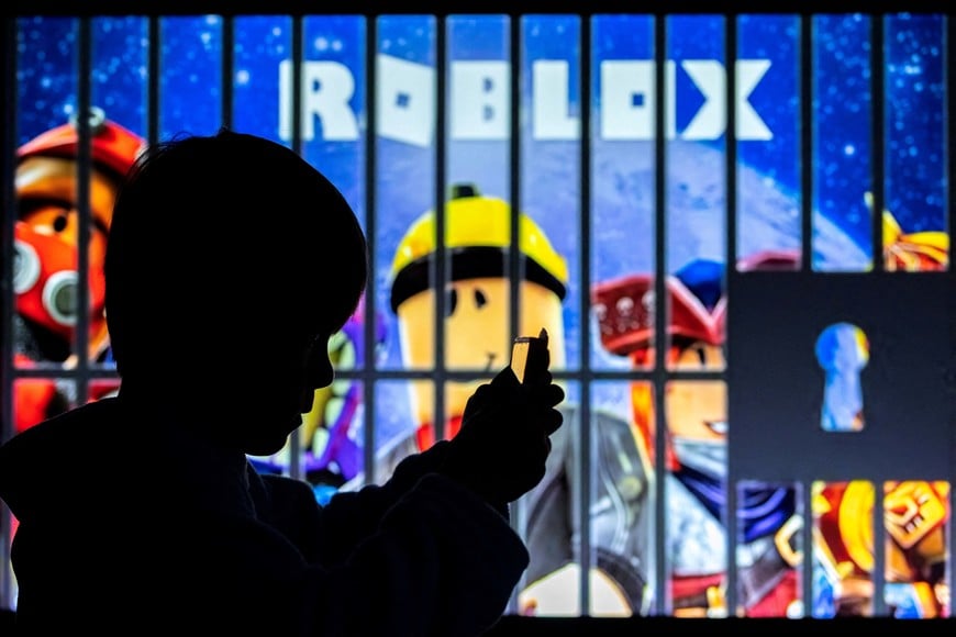 FILE PHOTO: A boy poses for a photo while holding a smartphone in front of a screen displaying characters of the U.S. children's video game Roblox, in this illustration taken December 8, 2025. REUTERS/Ramil Sitdikov/Illustration/File Photo