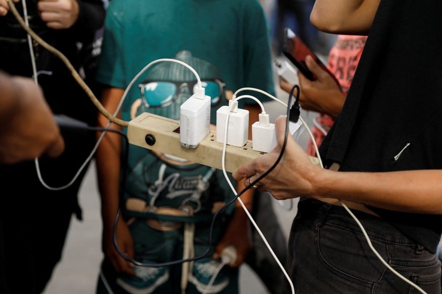 Sin sistema eléctrico, personas cargan sus teléfonos con un cable de extensión conectado a una farola luego del ataque. Crédito: REUTERS