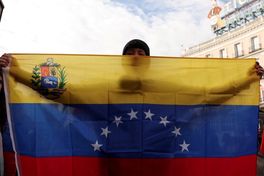 A person holds a state and naval Venezuelan ensign, as they react to the news after U.S. President Donald Trump said the U.S. has struck Venezuela and captured its President Nicolas Maduro, in Madrid, Spain, January 3, 2026. REUTERS/Violeta Santos Moura