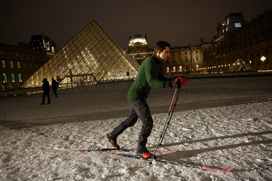 A man skis on the snow-covered courtyard in front of the glass Pyramid of the Louvre Museum in Paris, as winter weather with snow and cold temperatures hits a large part of the country, France, January 5, 2026. REUTERS/Abdul Saboor