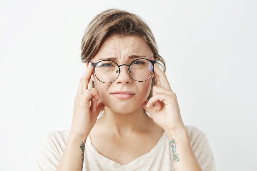 Young pretty girl in glasses thinking frowning looking at camera with fingers on temples over white background. Copy space.