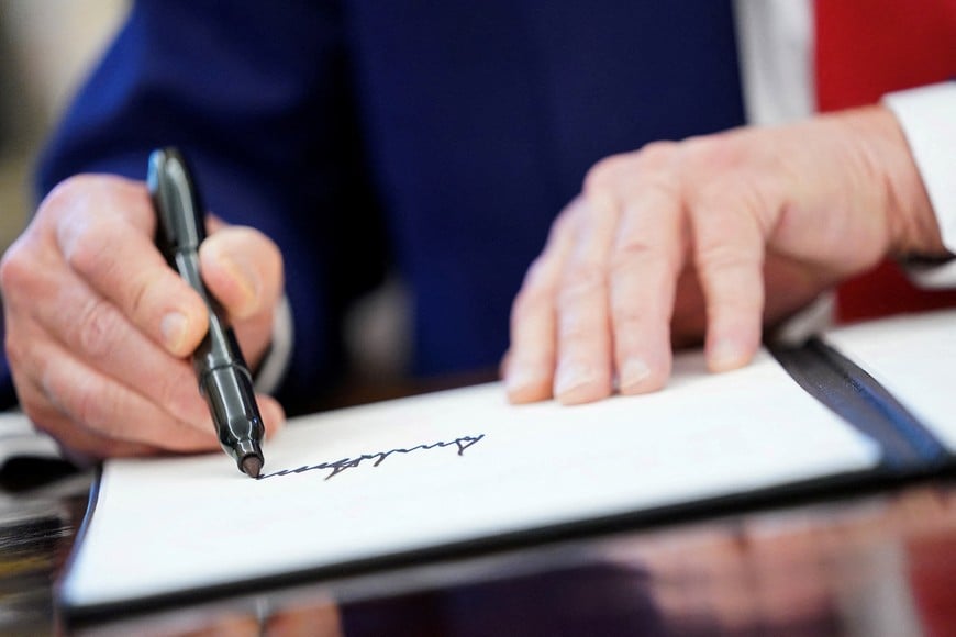 FILE PHOTO: U.S. President Donald Trump writes his signature, as he signs executive orders and proclamations in the Oval Office at the White House in Washington, D.C., U.S., April 9, 2025. REUTERS/Nathan Howard/File Photo