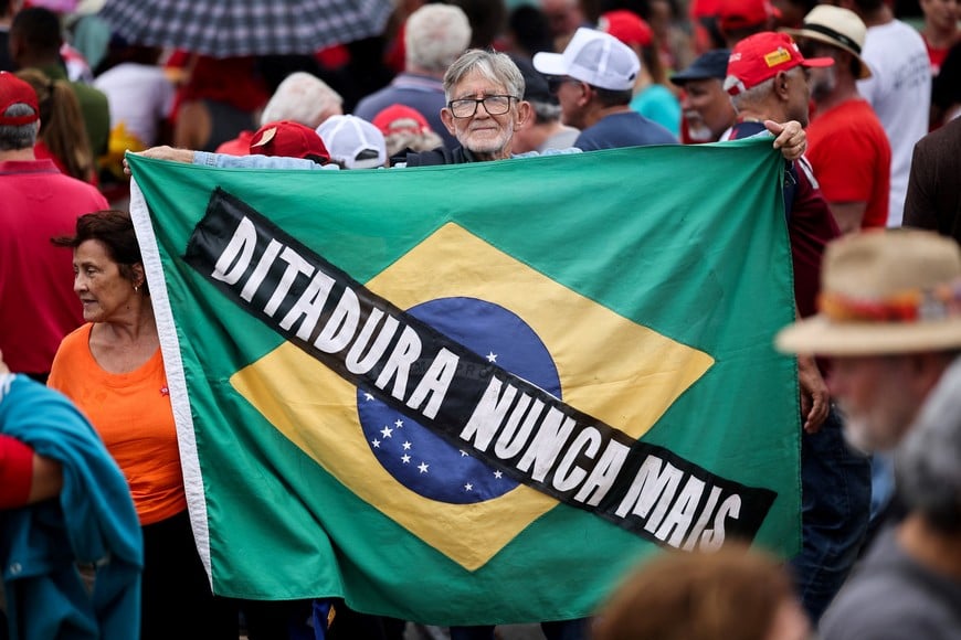 A man holds a Brazilian flag with a slogan reading "Dictatorship never again", after Brazil's President Luiz Inacio Lula da Silva vetoed a bill that would reduce former President Jair Bolsonaro's prison sentence during a ceremony marking the third anniversary of Bolsonaro's failed coup attempt, in Brasilia, Brazil January 8, 2026. REUTERS/Mateus Bonomi