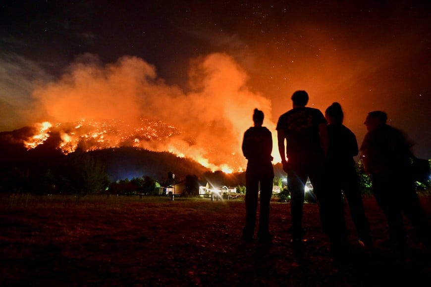 People look at smoke and flames rising from trees as a wildfire develops, in El Hoyo, in the Patagonian province of Chubut, Argentina January 7, 2026. REUTERS/Maxi Jonas