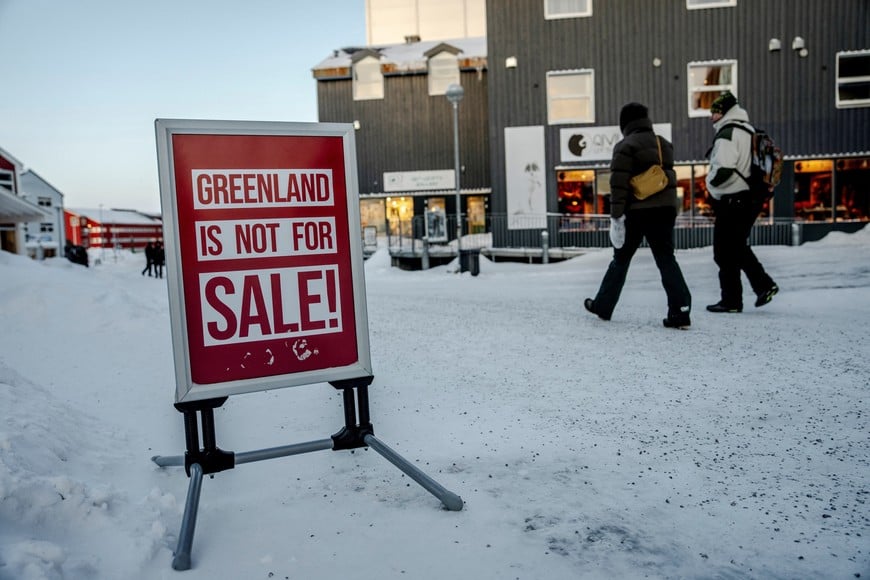 People walk past a sign placed on a street in Nuuk, Greenland, Tuesday, January 20, 2026. Ritzau Scanpix/ Mads Claus Rasmussen via REUTERS    ATTENTION EDITORS - THIS IMAGE WAS PROVIDED BY A THIRD PARTY. DENMARK OUT. NO COMMERCIAL OR EDITORIAL SALES IN DENMARK.