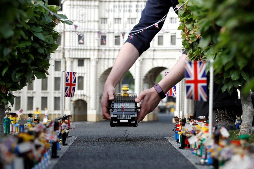 Legoland modeller Freya Groom poses for a photograph while placing a model of Britain’s Queen Elizabeth in a vehicle near a model of Admiralty Arch in The Mall, at Legoland in Windsor, Britain, May 31, 2022.  REUTERS/Peter Nicholls