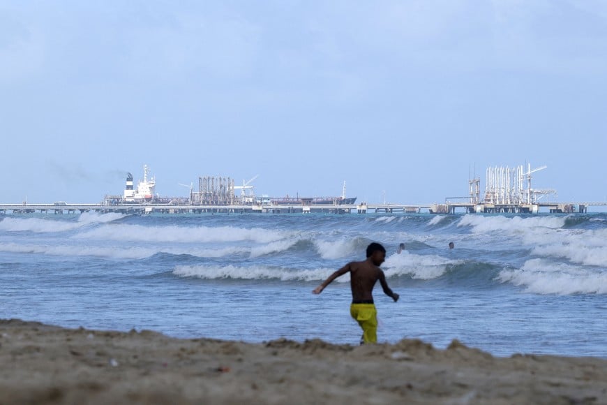 FILE PHOTO: People enjoy the ocean as an oil tanker is anchored near the El Palito refinery of Venezuelan state oil company PDVSA, after the National Assembly approved a major reform of the country's main oil law, in Puerto Cabello, Venezuela, January 27, 2026. REUTERS/Gaby Oraa/File Photo