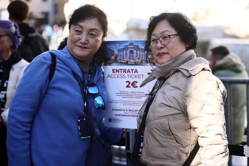 Tourists pose next to a sign indicating the newly introduced two-euro paid entry at the Trevi Fountain, as well as several other monuments and museums that were previously free, in Rome, Italy, February 2, 2026. REUTERS/Vincenzo Livieri
