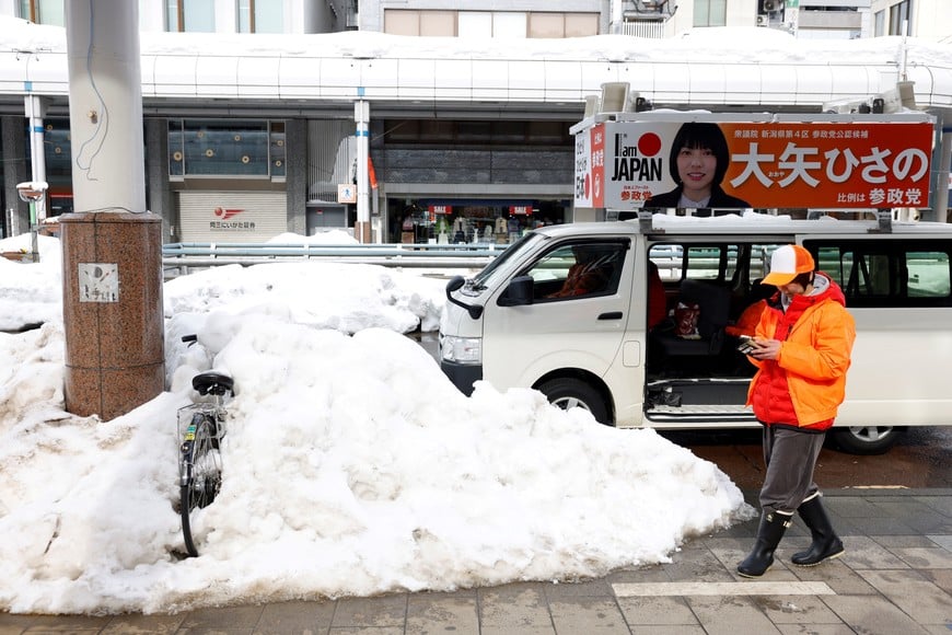 A supporter of Hisano Oya, a candidate from the Sanseito, walks on a snow-covered street next to a vehicle displaying an Oya banner, ahead of the February 8 snap election, in Nagaoka, Japan, February 7, 2026. REUTERS/Manami Yamada
