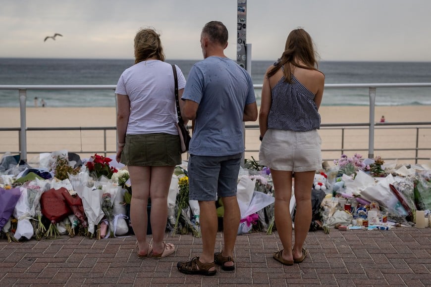 People stand in front of flowers offered to honour the victims of a mass shooting during a Jewish Hanukkah celebration at Bondi Beach on December 14, in Sydney, Australia, December 19, 2025. REUTERS/Eloisa Lopez