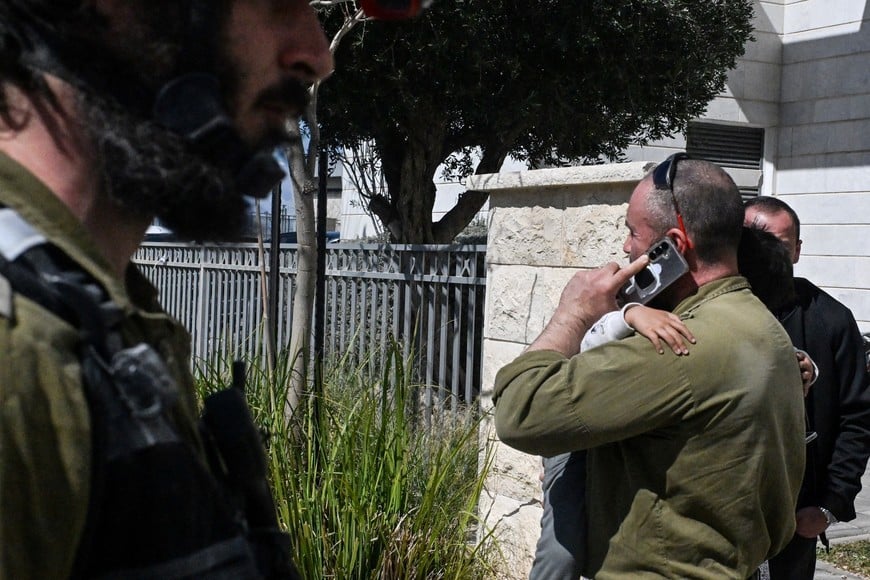 An Israeli soldier speaks on the phone while holding his child during the partial evacuation of a residential building damaged by shrapnel, after missiles were launched towards Israel from Iran following strikes by Israel and the U.S. on Iran, in Haifa, northern Israel, February 28, 2026. REUTERS/Rami Shlush    ISRAEL OUT. NO COMMERCIAL OR EDITORIAL SALES IN ISRAEL