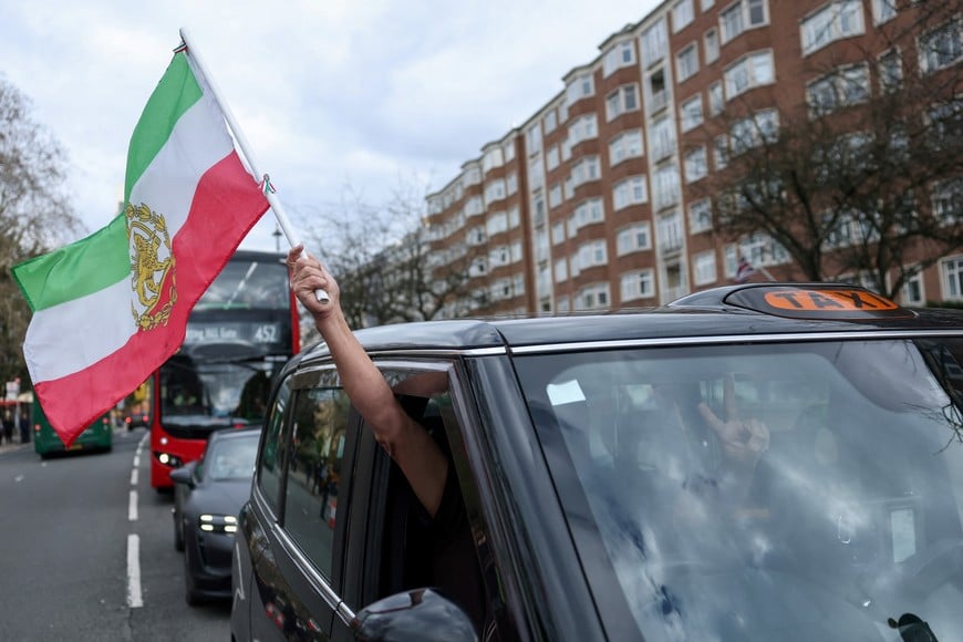 A taxi driver holds a "Lion and Sun" pre-Iranian revolution flag out of his cab, as people attend a demonstration in support of military action against the Iranian regime, following strikes by the U.S. and Israel against Iran, outside the Iranian embassy in London, Britain, February 28, 2026. REUTERS/Toby Melville