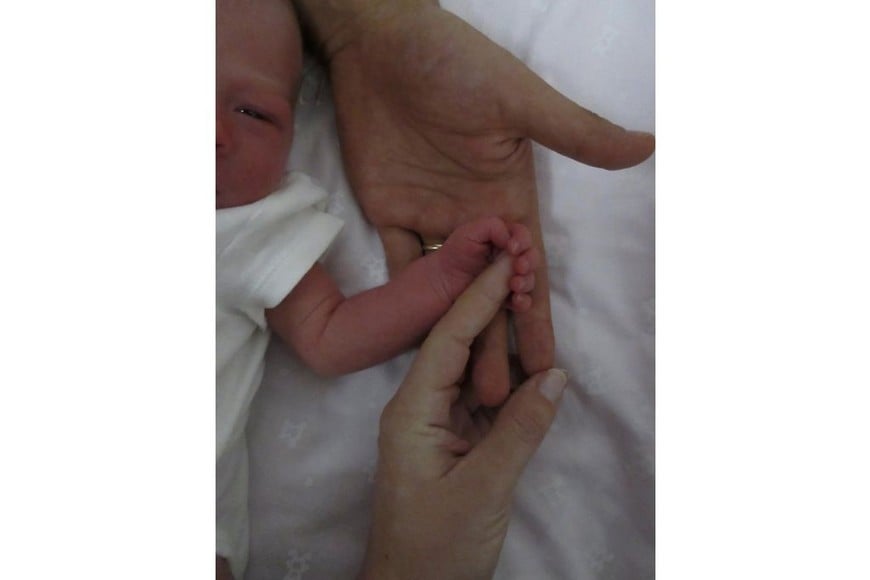 En la imagen se alcanza a percibir solo un lado del rostro de la bebé, junto con su pequeña mano que sostiene el dedo de Oriana y debajo, la mano de Paulo.