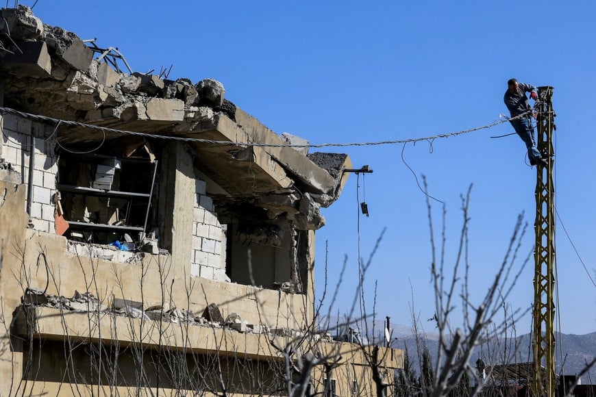 A man works on an electric pole next to a damaged building, in the aftermath of an Israeli strike on Friday, in Tamnine el Tahta, Bekaa valley, Lebanon, February 21, 2026. REUTERS/Mohamed Azakir     TPX IMAGES OF THE DAY