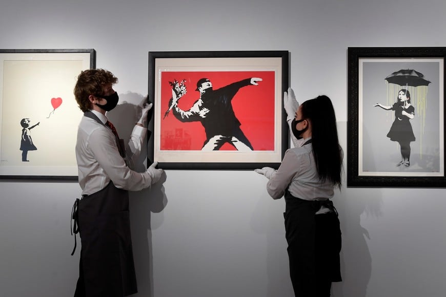 Art handlers pose as they hold 'Love is in the Air' by Banksy which forms part of an upcoming online auction at Christie's entitled 'Prints and Multiples and Banksy: I Can't Believe You Morons Actually Buy This Sh*t', London, Britain, March 26, 2021. REUTERS/Toby Melville NO RESALES. NO ARCHIVES