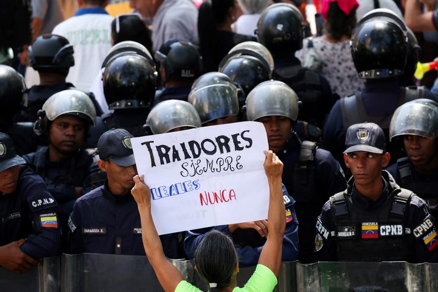 A woman holds a sign reading "Traitors always, loyal never" in front of a Bolivian National Police barricade as public sector workers protest to demand higher wages and better working conditions in Caracas, Venezuela March 23, 2026. REUTERS/Leonardo Fernandez Viloria