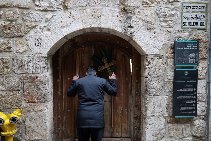 Issa Kassissieh, a Palestinian Christian who is popular for being the Santa Claus of the city, holds a cross and a palm frond while standing at the doors of the Church of the Holy Sepulchre after finding it is locked, following the cancellation of the traditional Palm Sunday procession from the Mount of Olives, amid restrictions on gathering in large groups and the U.S.-Israel conflict with Iran, in Jerusalem's Old City March 29, 2026. REUTERS/Ammar Awad