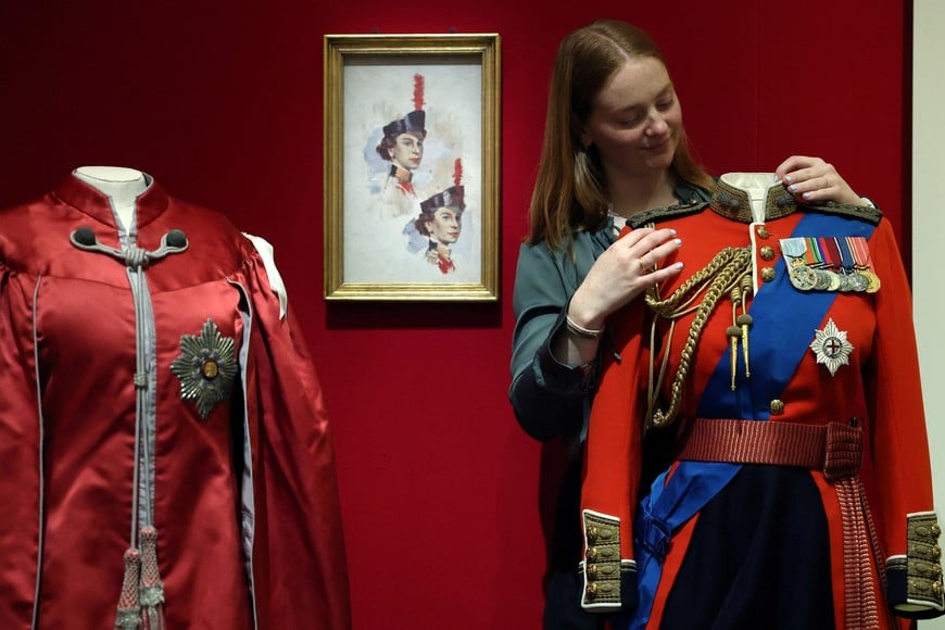 Royal Collection Trust exhibitions manager Laura Drew  poses with a full dress tunic used on horseback during ceremonial events which forms part of "Queen Elizabeth II: Her Life in Style", an exhibition of clothing and outfits marking the centenary of the late queen’s birth, in The King’s Gallery at Buckingham Palace, London, Britain, April 9, 2026. REUTERS/Toby Melville