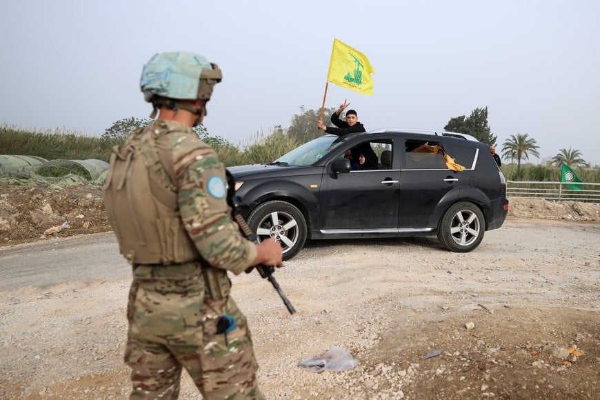 A boy waves a Hezbollah flag from a vehicle infront of a UN peacekeeper as displaced people make their way back to their homes crossing the bridge linking southern Lebanon to the rest of the country, which was hit earlier in an Israeli strike, after a 10-day ceasefire between Lebanon and Israel went into effect, in Qasmiyeh, Lebanon, April 18, 2026. REUTERS/Louisa Gouliamaki