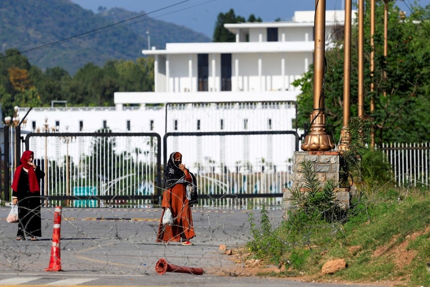 Women walk along a road blocked with barbed wire for security measures, with the President's House in the background, as Pakistan prepares to host the United States and Iran for the second phase of peace talks, in Islamabad, Pakistan, April 19, 2026. REUTERS/Akhtar Soomro