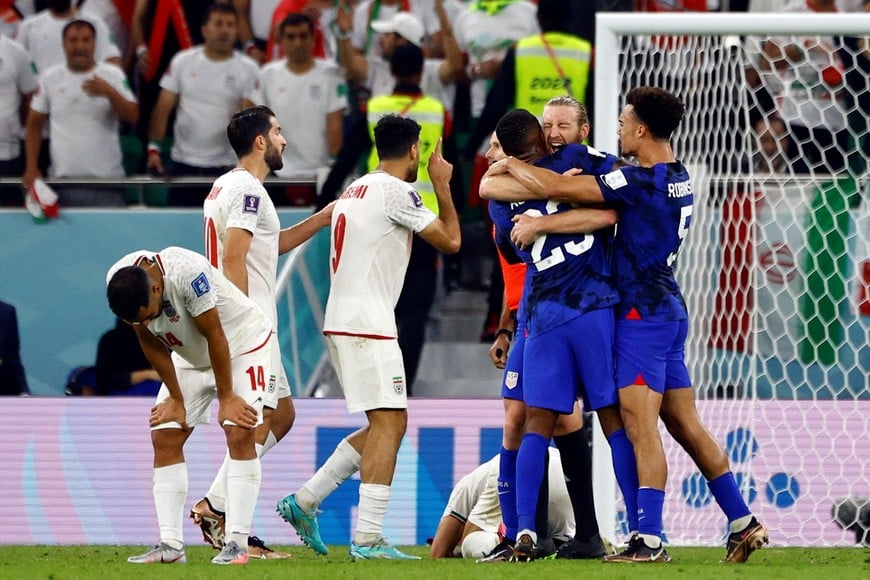Soccer Football - FIFA World Cup Qatar 2022 - Group B - Iran v United States - Al Thumama Stadium, Doha, Qatar - November 30, 2022
Iran's Saman Ghoddos looks dejected after the match as Iran are eliminated from the World Cup and United States players celebrate qualifying for the knockout stages REUTERS/Susana Vera