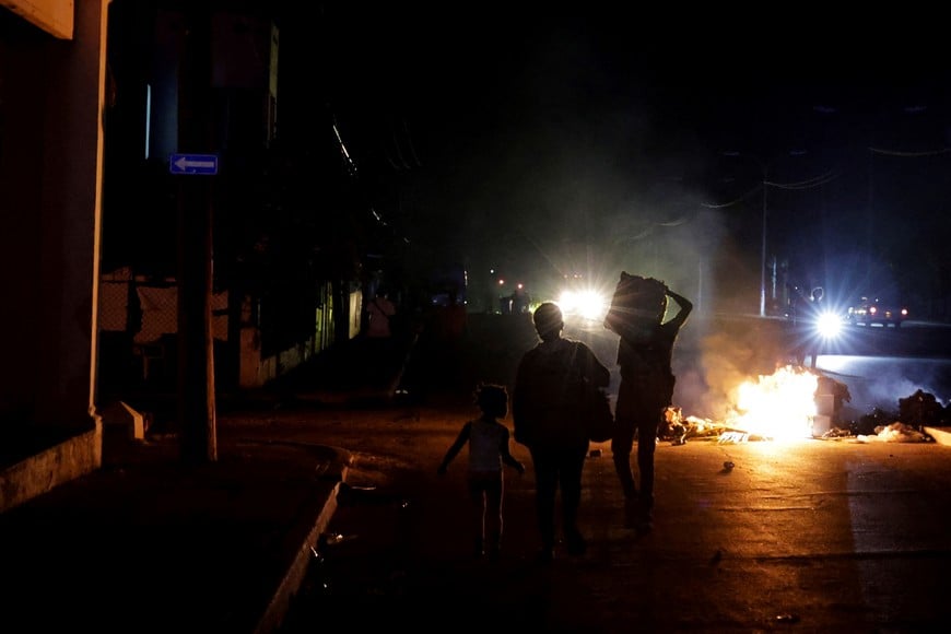 People walk past trash set on fire in the middle of a street during a protest against frequent power cuts as Havana faces its worst rolling blackouts in decades amid a U.S. blockade that has strangled the island of fuel, in Havana, Cuba, May 13, 2026. REUTERS/Norlys Perez