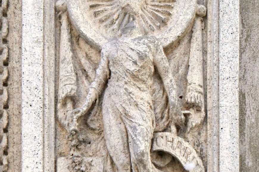 Dos divinidades femeninas con evocaciones cristianas. La de la izquierda está acompañada por un angelito que sostiene una cartela con la palabra Fide (Fe). La de la derecha, que emblematiza la Caridad (Charitas), lamentablemente, ha perdido su cabeza.