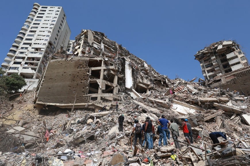 (260626) -- LA GUAIRA, 26 junio, 2026 (Xinhua) -- Personas son vistas sobre los escombros de edificios derrumbados luego de que se registraran dos terremotos, en Catia La Mar, estado La Guaira, Venezuela, el 26 de junio de 2026. Aumentó a 920 la cifra de las personas fallecidas a causa de los dos sismos de magnitud superior a 7 en la escala de Richter registrados el pasado 24 de junio en Venezuela, confirmó el viernes el presidente de la Asamblea Nacional, Jorge Rodríguez. (Xinhua/Marcos Salgado) (ms) (ra) (vf)