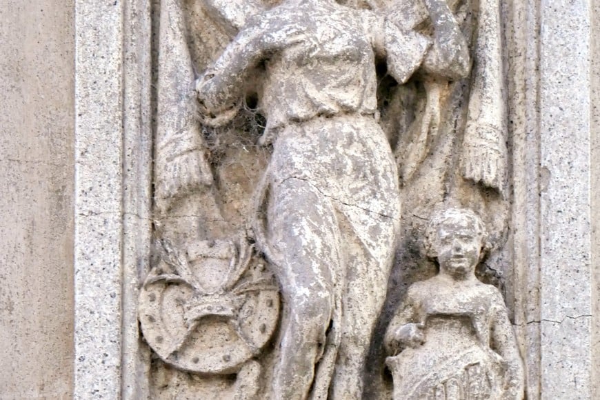 Dos divinidades femeninas con evocaciones cristianas. La de la izquierda está acompañada por un angelito que sostiene una cartela con la palabra Fide (Fe). La de la derecha, que emblematiza la Caridad (Charitas), lamentablemente, ha perdido su cabeza.