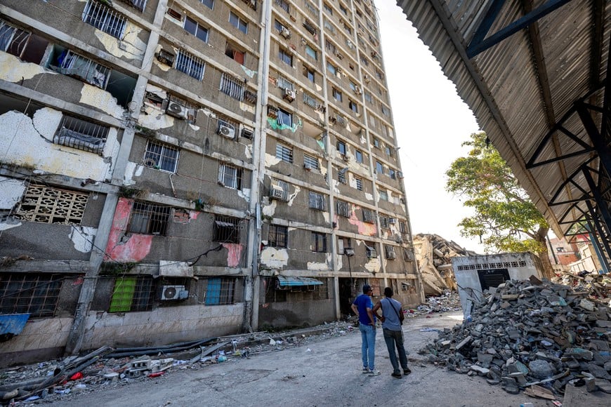 Locals stand next to a damaged building in Catia La Mar, La Guaira state, Venezuela, on June 29, 2026. Hopes were fading on June 29, 2026 of finding survivors more than four days after powerful twin earthquakes struck Venezuela, as residents grow increasingly frustrated with the government's response to the disaster that has killed at least 1,450 people and left tens of thousands unaccounted for.     MIGUEL MEDINA/Pool via REUTERS
