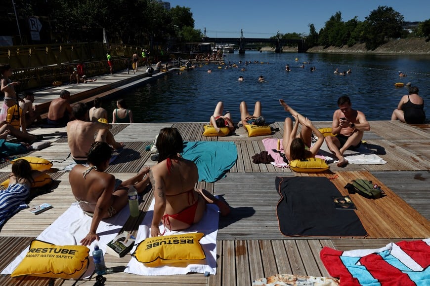 People sunbath on a jetty as others swim in the River Seine at the Grenelle public bathing site, which is open to swimmers for the second year in the capital's historic waterway in Paris, France, July 4, 2026. REUTERS/Tom Nicholson