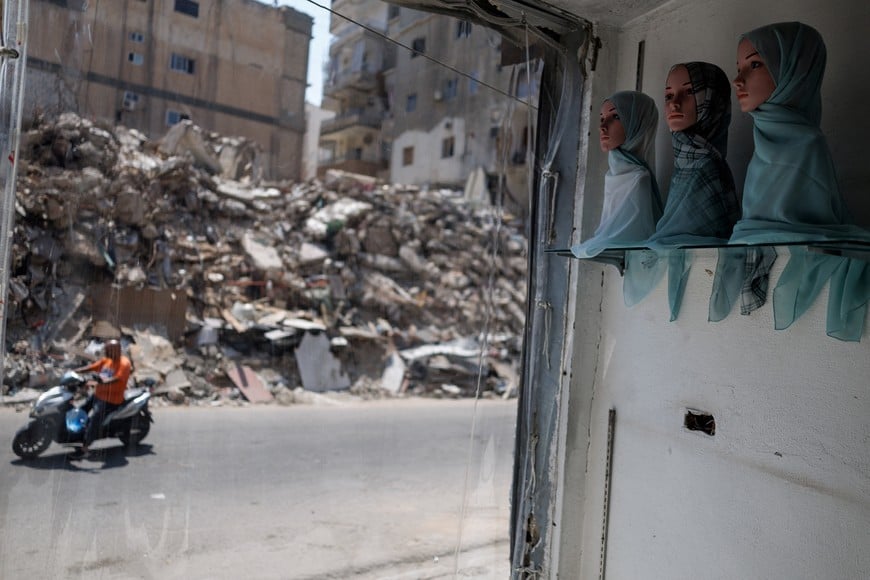 A motorcycle drives past as mannequin heads are displayed inside a reopened clothing store with blast-damaged windows, as rubble from a building destroyed in an Israeli strike is seen across the street, in Tyre, southern Lebanon, July 5, 2026. REUTERS/Zohra Bensemra