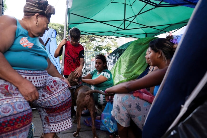 Displaced residents sit outside their tents while petting a dog after the housing complex where they live was damaged in the June 24 earthquakes and they were unable to return to their apartments, in Caracas, Venezuela, July 5, 2026. REUTERS/Marian Carrasquero