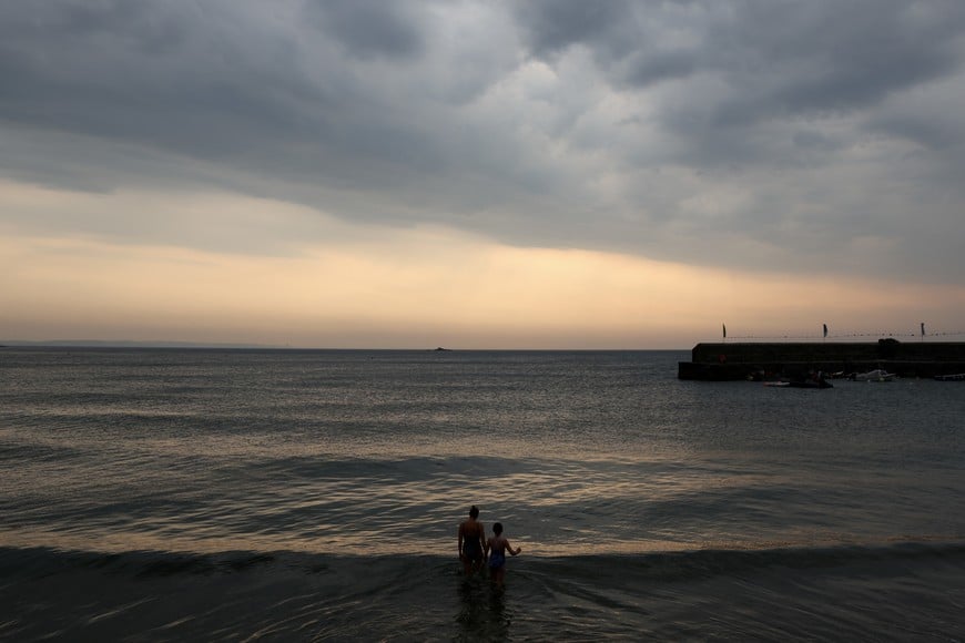 People swim in the sea as storm clouds bring rain, thunder and lightning to Gorran Haven in Cornwall, Britain, July 19, 2022. REUTERS/Tom Nicholson