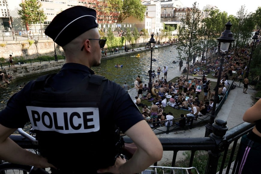 FILE PHOTO: Police watch as people swim in the Canal Saint-Martin after public swimming was permitted in certain areas due to high temperatures amid a heatwave in Paris, France, June 26, 2026. REUTERS/Tom Nicholson/File Photo